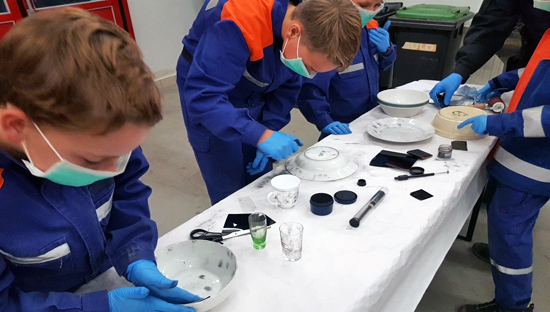 Jugendliche versuchen Fuß- und Fingerabdrücke sichbar zu machen mit Handschuhen und Maske