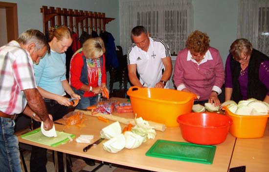 Mehrere Personen stehen an Tischen und reiben Kraut