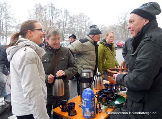 Personen unterhalten sich neben einem Tisch mit Glühwein, mit Tassen darauf