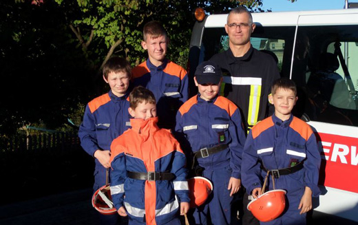 5 Kinder und 1 Erwachsener posieren vor einem Feuerwehrfahrzeug
