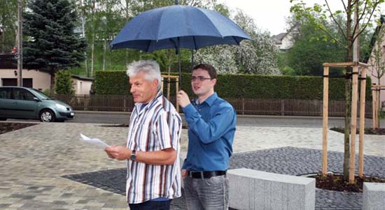 Mann hält einem anderen Mann, der eine Rede hält, den Regenschirm