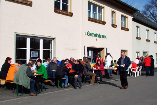 Vor dem gemeindeamt sitzten Menschen auf Bierbänken und essen Speckfett