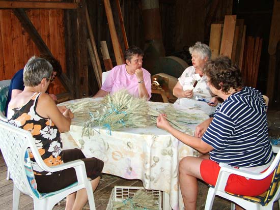 5 Frauen sitzen an einem Tisch und flechten das Korn zusammen