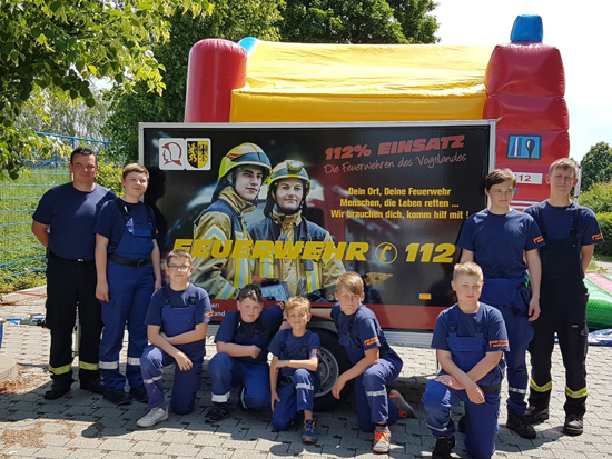Jugendfeuerwehr stehen vor einem Plakat an einer Hüpfburg