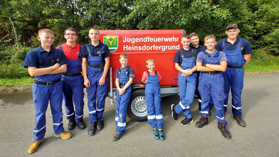 9 Kinder/Jugendliche stehen vor ihrem neuen Anhänger mit roter Plane