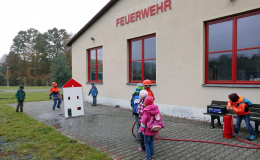 Kinder spielen neben dem Feuerwehrhaus mit Wasser