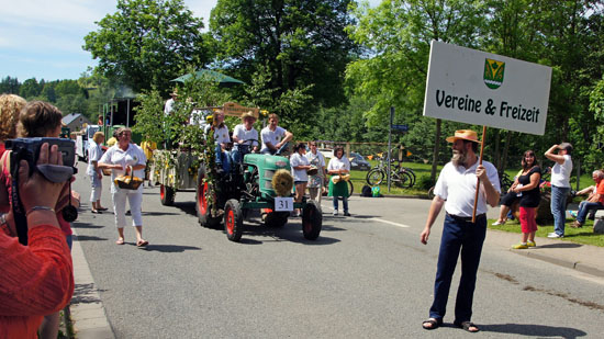 Traktor festlich geschmückt, mit einem Mann vorauslaufend mit Schild in der Hand