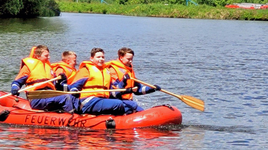 4 Kinder auf einem roten Paddelboot und gelben Schwimmwesten