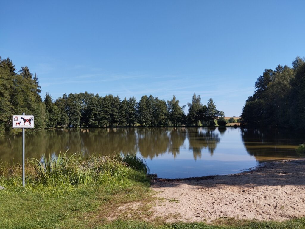 Blick auf den Mühlenteich mit kurzem Strandabschnitt und Schild daneben