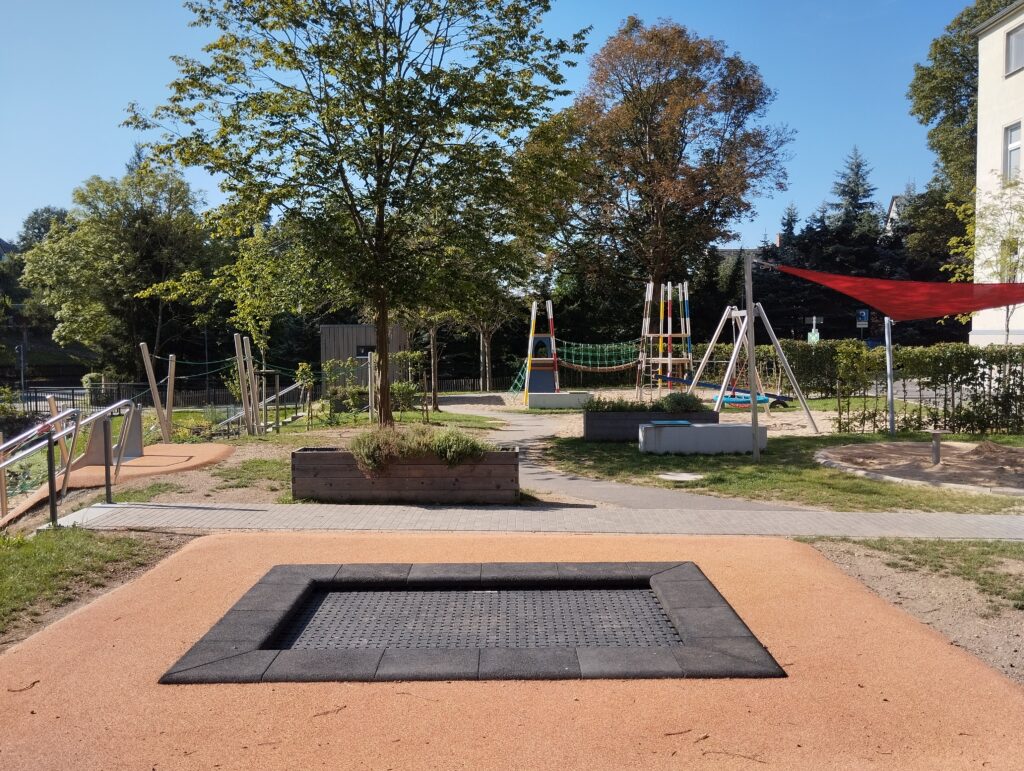 Trampolin auf Spielplatz mit Rutsche im Hintergrund
