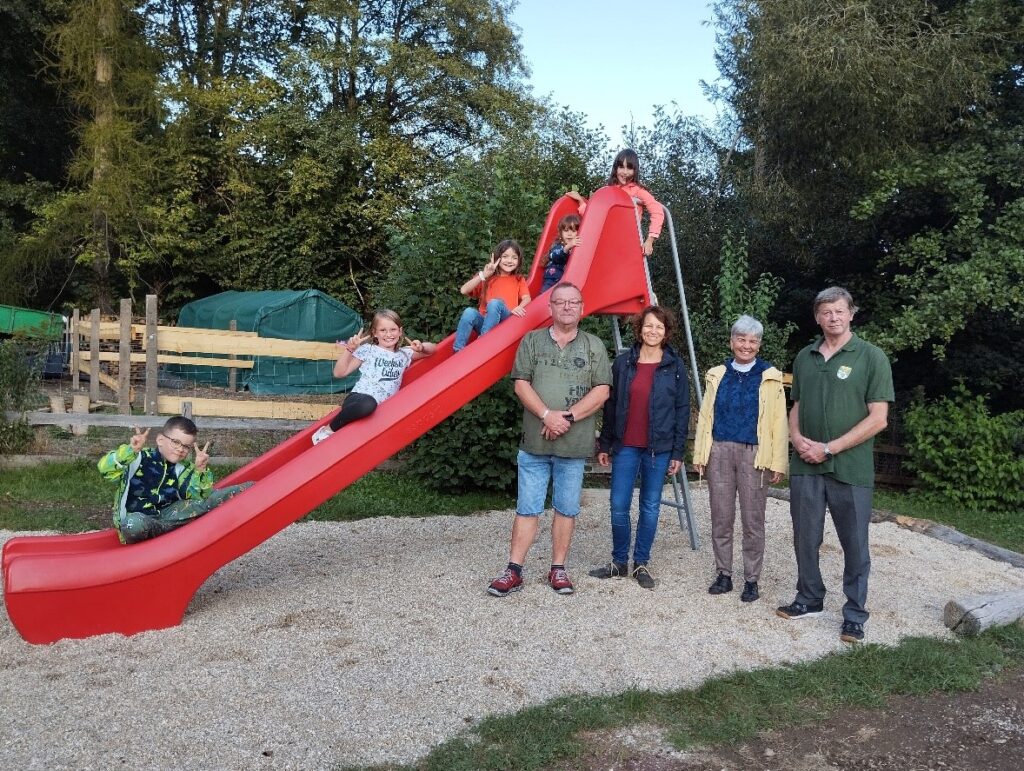Kinder und Erwachsene stehen um die neue rote Rutsche herum