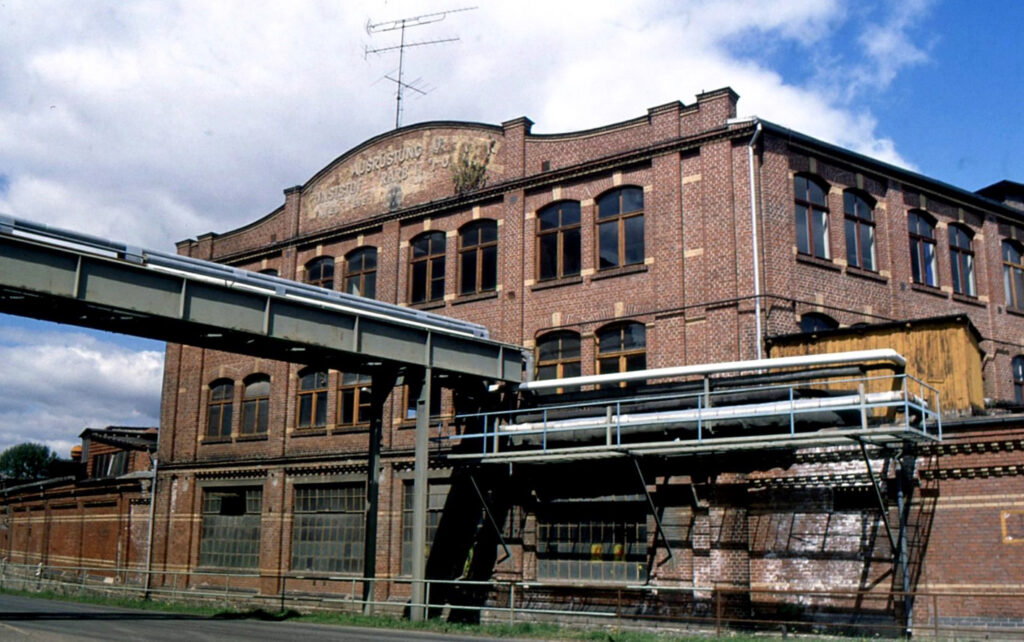 Industriehalle mit Rohren, die zum braunen Gebäude führen