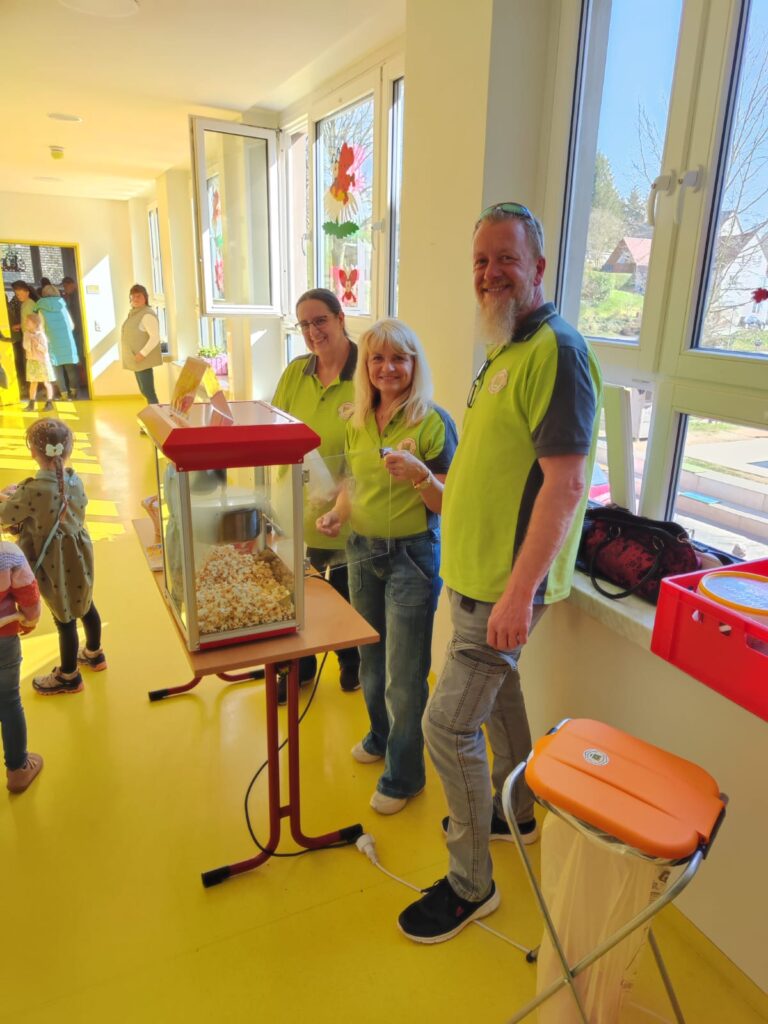 3 Mitglieder des Heimatverein am Tisch mit Popcornmaschine auf dem Flur der Grundschule Hauptmannsgrün