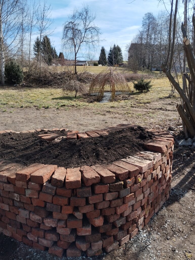 Auf dem Bild ist das Gelände des Dorfgartens zu sehen. Im Vordergrund die angelegte Kräuterschnecke und im Hintergrund das gebaute Weideniglu.
